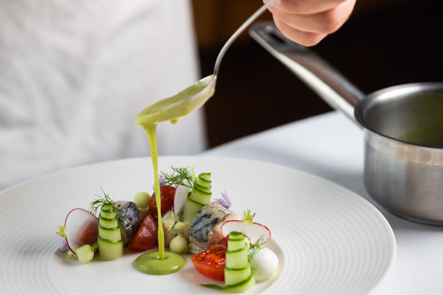 De kok maakt een culinair gerecht af met een lepel.