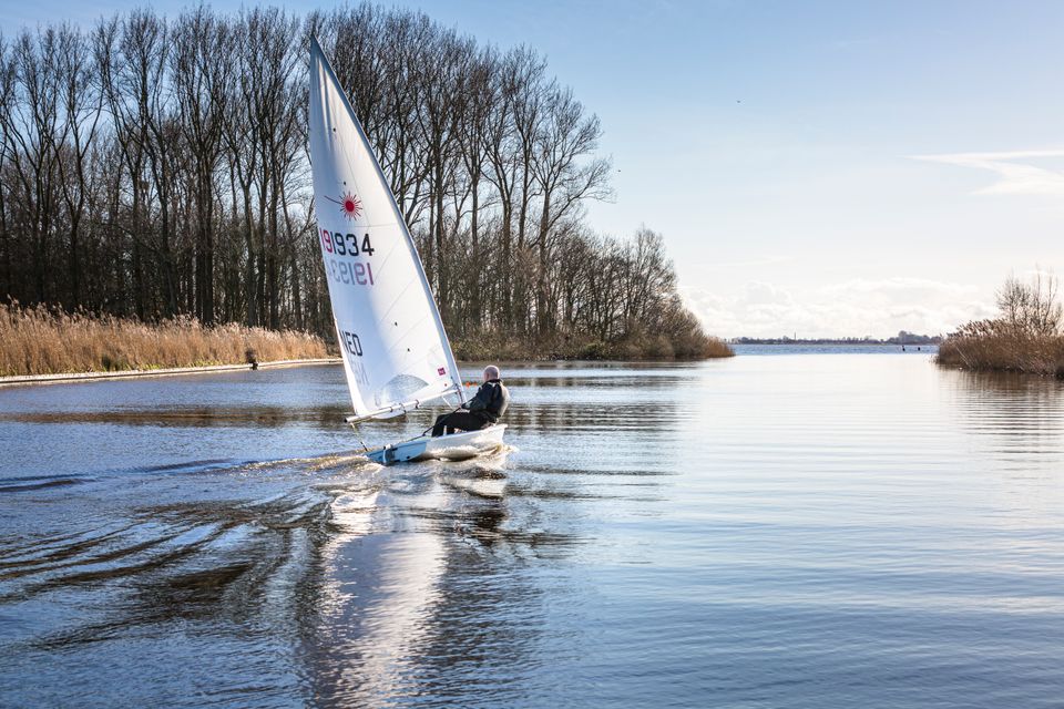 Een zeilbootje zeilt s'winters perfecte boeglijnen over het spiegelachtige water.