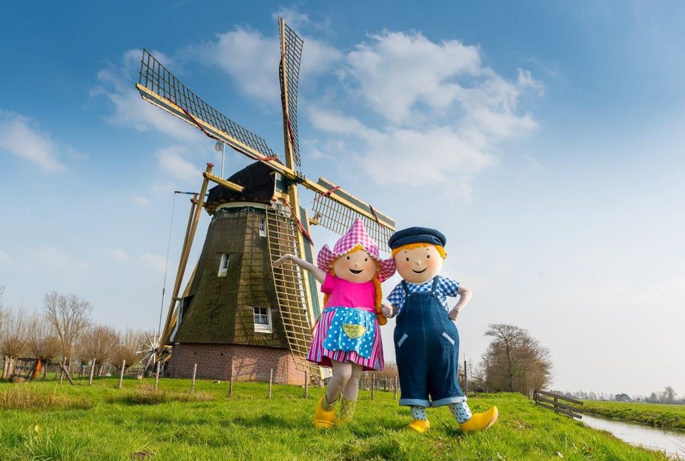 Twee boerenpoppen poseren voor een windmolen in het polderlandschap bij Avonturenboerderij Molenwaard.