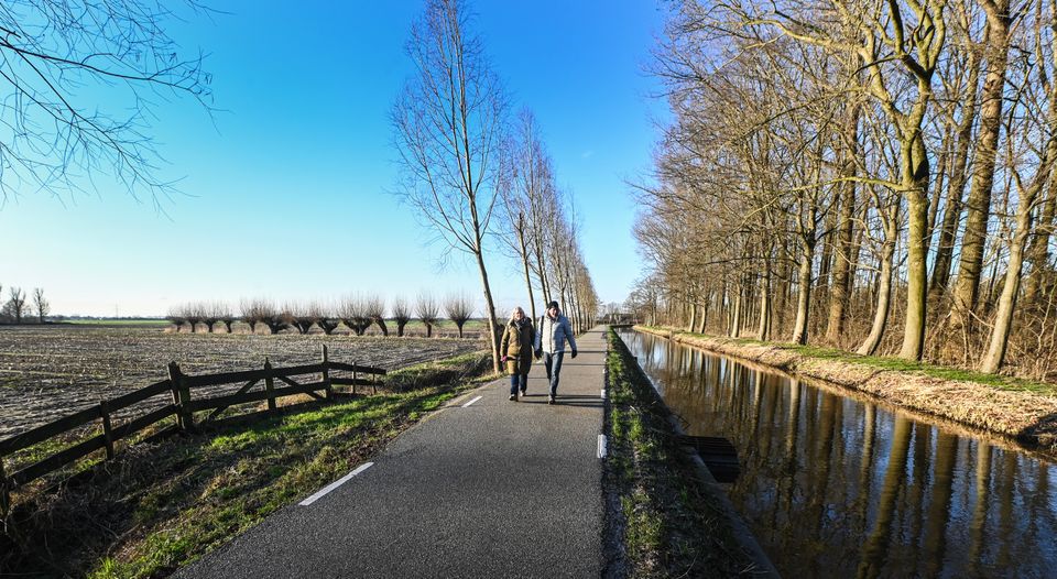 Twee wandelaars lopen over een rustig pad langs het water in Linschoten, omgeven door kale bomen en winterse polderlandschappen in het Groene Hart.