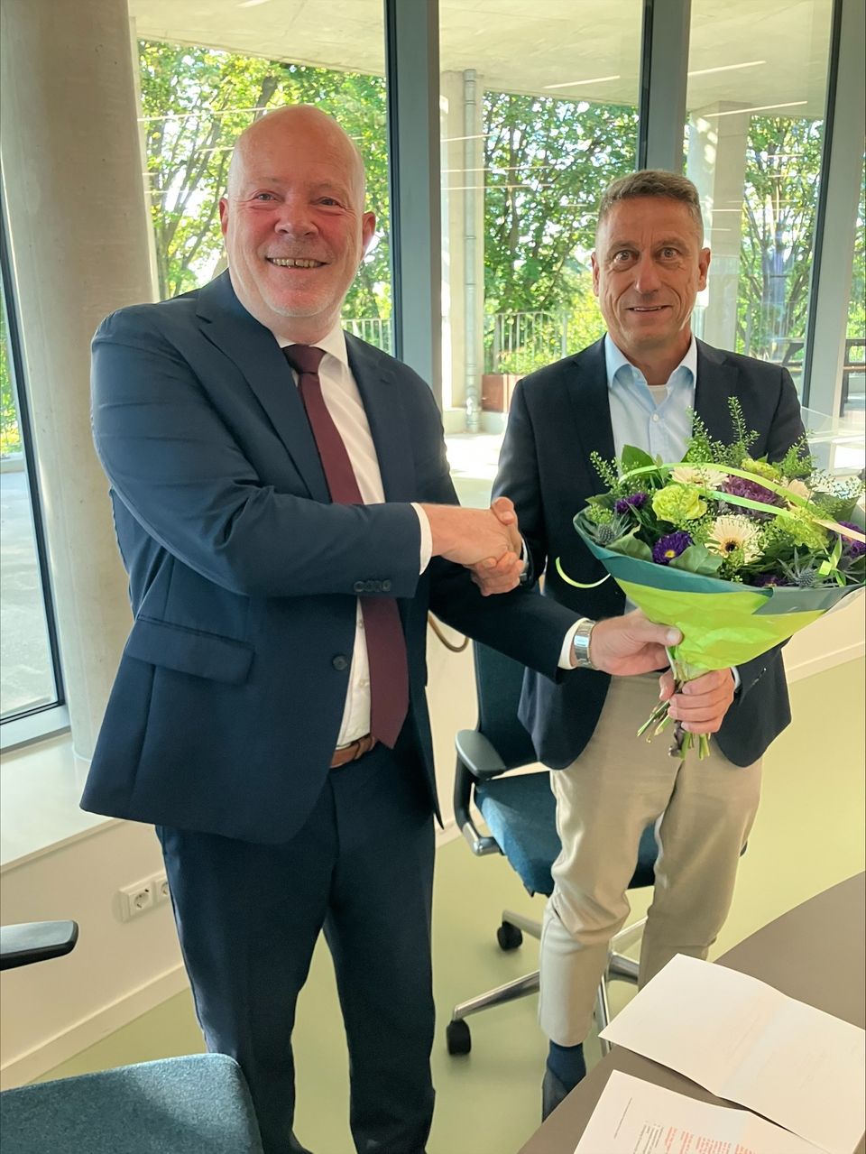 Fotobijschrift: Wethouder Robert Simons (links) neemt bloemen in ontvangst van Aart Jan Spoon (rechts), waarnemend voorzitter van het Samenwerkingsverband Wonen regio Rotterdam (SvWrR), ter gelegenheid van zijn benoeming tot nieuwe voorzitter.
