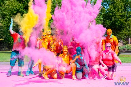 Het vrijwilligersteam van de Woerdense VakantieWeek poseert voor een foto tijdens de Colorrun met overal kleurpoeder en bomen op de achtergrond.