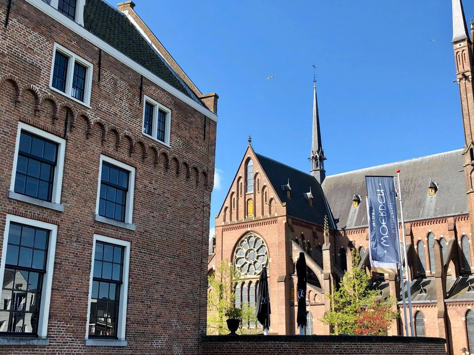 Kerkgebouw Sint-Bonaventurakerk in Woerden, Groene Hart. Historische neogotische kerk met hoge spits, roosvenster en bakstenen gevels in het centrum van Woerden onder een heldere blauwe lucht.