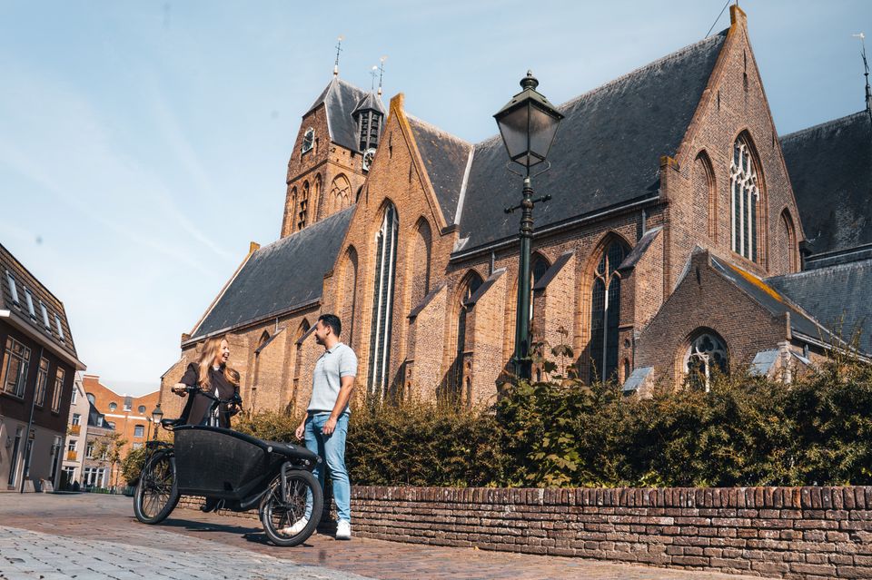 Historische kerk Grote of Sint-Michaëlskerk in Oudewater, Groene Hart. Bezoekers met bakfiets op de straat voor de monumentale gotische kerk in de historische binnenstad, populair voor fietsen, wandelen en stedentrips.