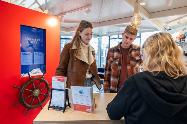 Twee bezoekers in gesprek met een baliemedewerkers bij het VVV Bezoekerscentrum in Stavoren.