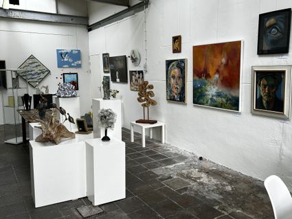 Kunstgalerie tijdens Atelierroute Woerden in Woerden, Groene Hart, expositieruimte met schilderijen, portretten en abstracte kunst aan witte muren en verschillende beelden en sculpturen op sokkels.