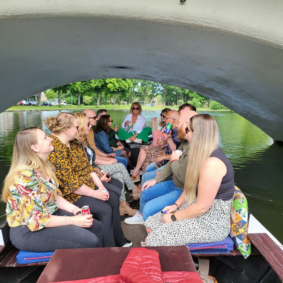 Rondvaartboot Sweet Caroline in Woerden, Groene Hart. Groep deelnemers geniet van een openluchtvaart door de stad terwijl de boot onder een brug door vaart, populair als groepsuitje, bedrijfsuitje en vaartocht over de Woerdense Singel.