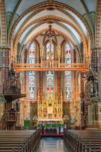 Kerkinterieur van de Sint-Franciscuskerk in Oudewater, Groene Hart. Neogotische katholieke kerk met rijk versierd hoogaltaar, glas-in-loodramen, kruisbeeld, gewelfde plafonds en symmetrisch zicht vanaf het middenschip.