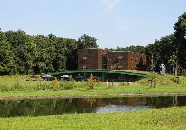 Buitenkant van Boshotel Overberg, omringd door groen en met een vijver op de voorgrond. Het moderne hotel ligt in een rustige, natuurlijke omgeving op de Utrechtse Heuvelrug.