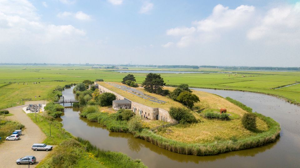 Het Fort bij Krommeniedijk gefotografeerd vanuit de lucht. Op de voorgrond zie je een aantal auto's op de parkeerplaats en op de achtergrond zie je uitgestrekte weilanden.