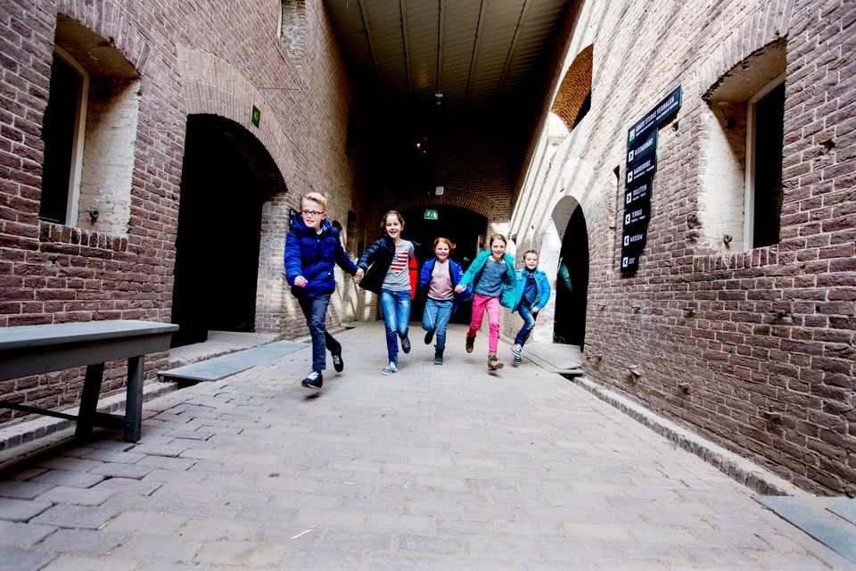 Een groep kinderen rent door een gang met veel licht door een lichtstraat in het plafond.