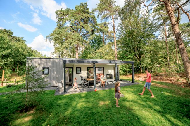 Vader en dochter spelen in de ruime tuin van chalet Zuylestein bij RCN het Grote Bos. Het moderne vakantiehuis ligt op een groene en bosrijke plek.