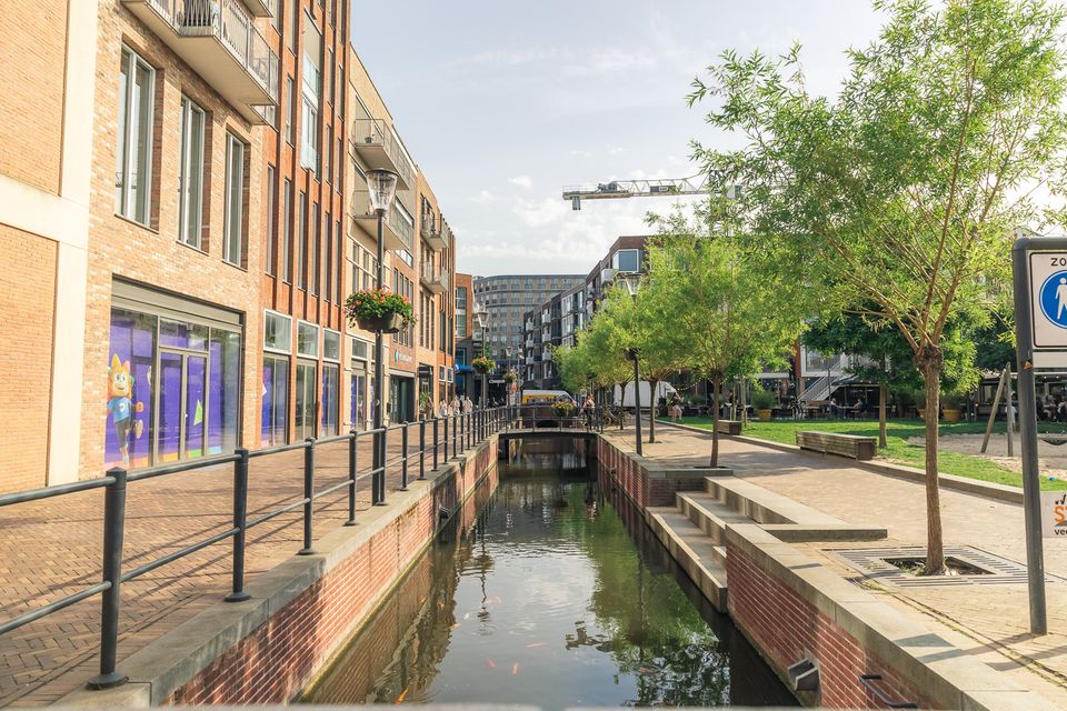 Moderne binnenstad van Veenendaal met winkels, woningen, groen en een watergang door het centrum. De foto laat de combinatie van winkelen, verblijven en openbare ruimte in het stadscentrum zien.