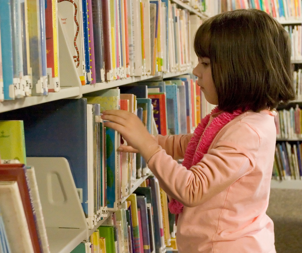 Meisje zoekt een boek uit in de bibliotheek.