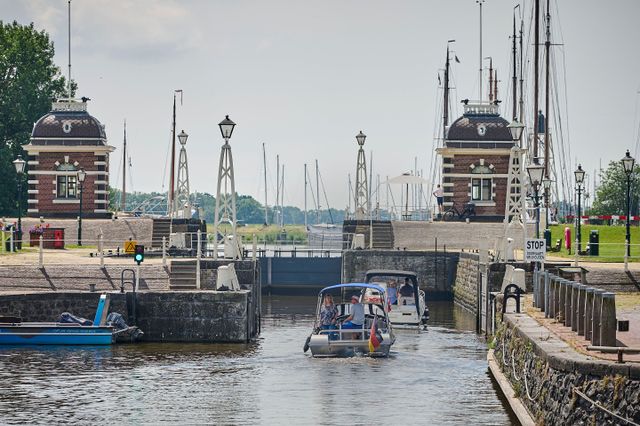 Twee boten varen in de sluis van Lemmer. Op de achtergrond staan masten van zeilboten.