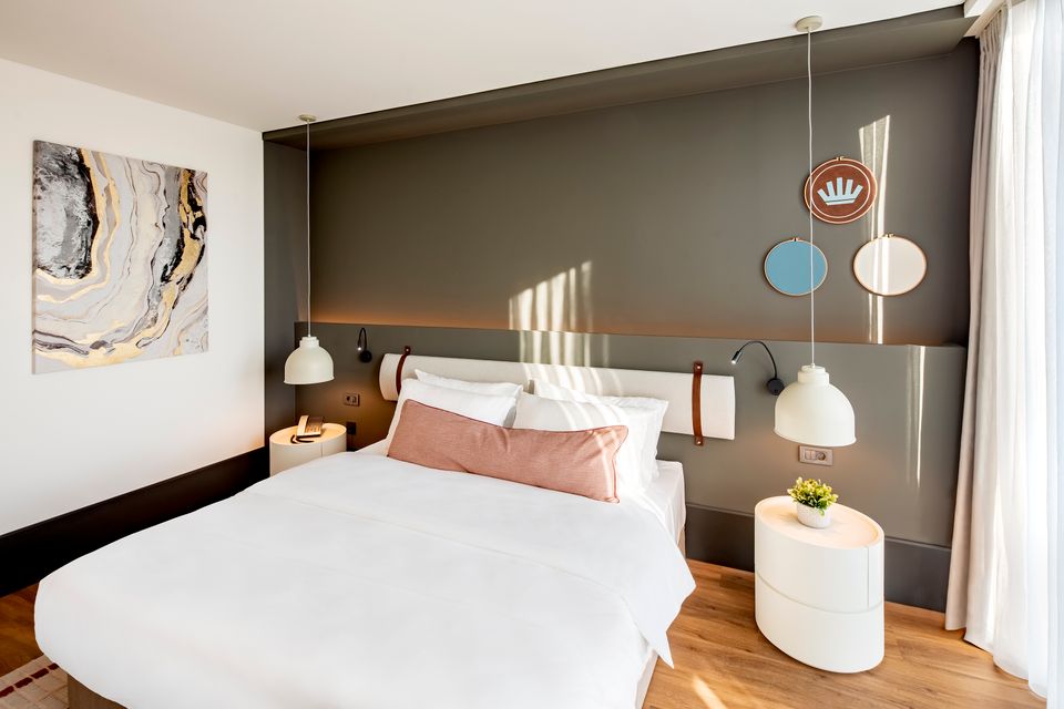 Foto van een moderne hotelkamer met een groot bed in het midden tegen een donkere achtergrond.